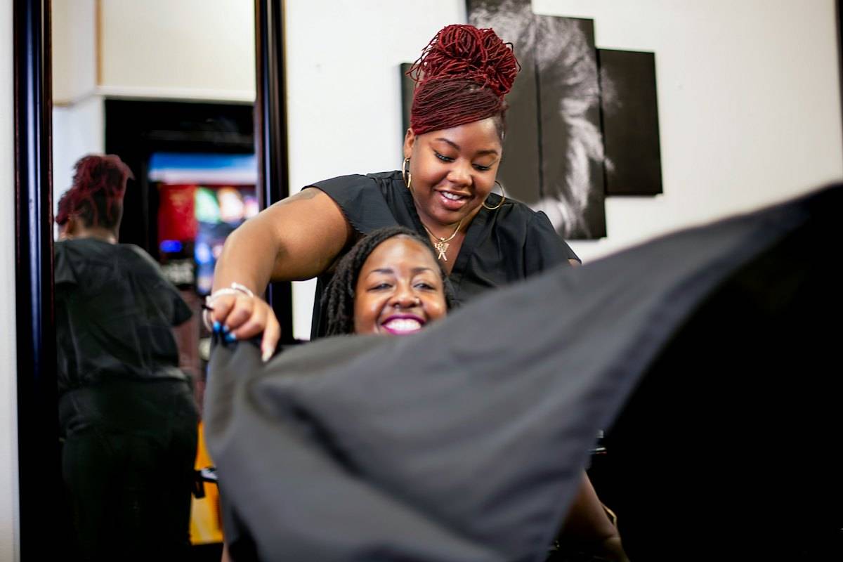 Barber smiling as she drapes a cape over a client