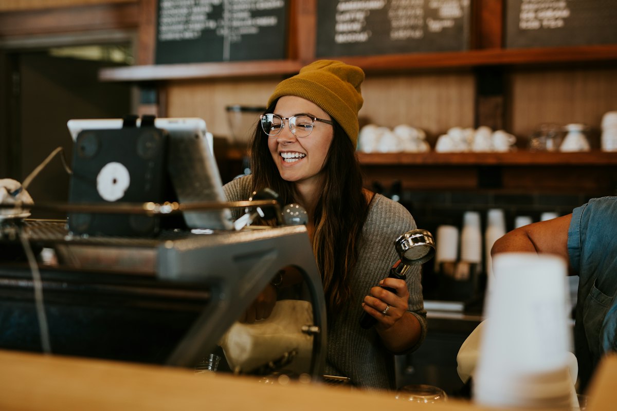 A smiling barista holding a portafilter behind a coffee bar