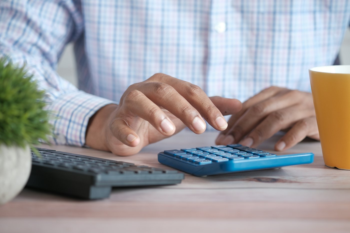 A hand using a calculator on a desk next to a coffee mug