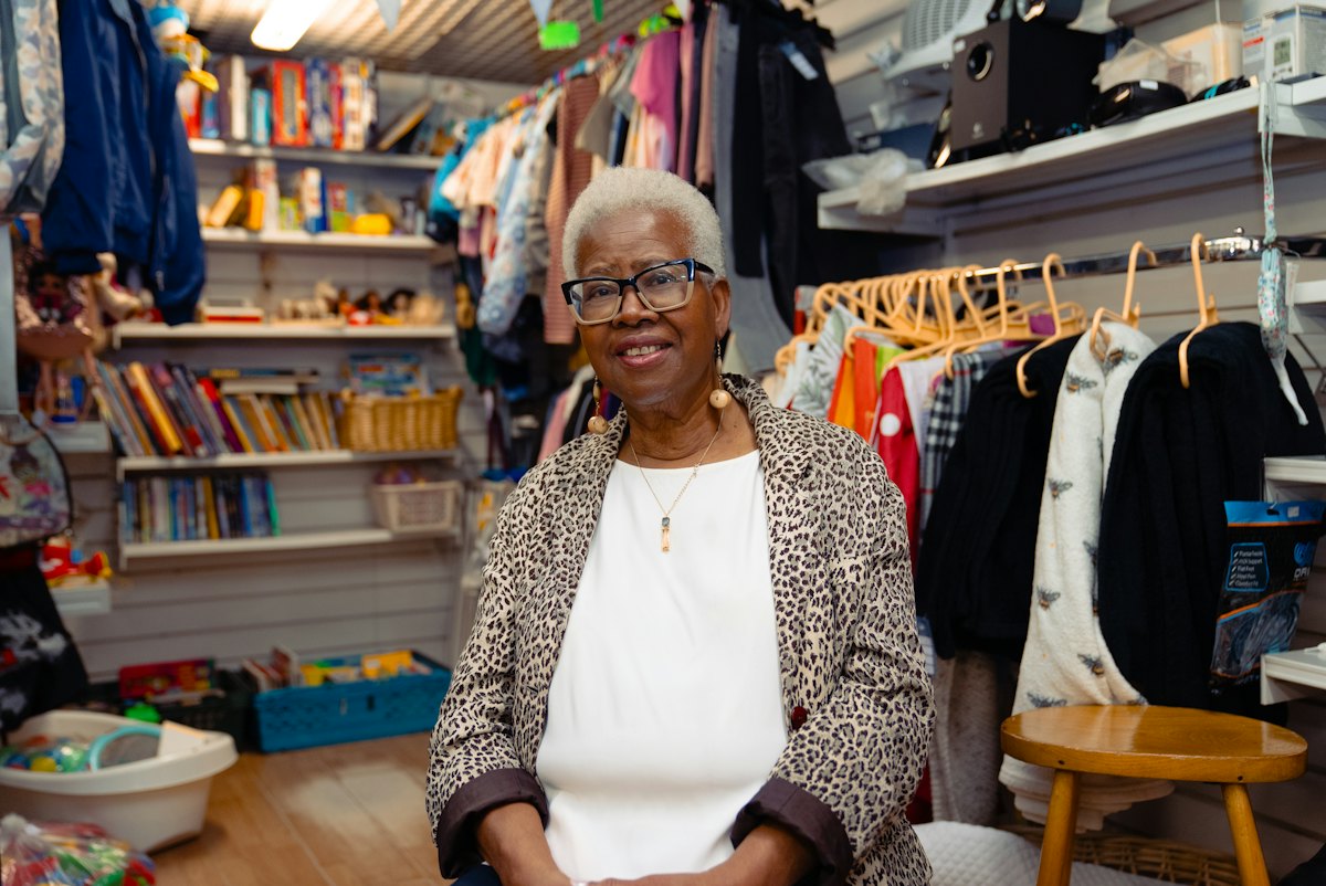 An older woman smiling in a small clothing and book shop