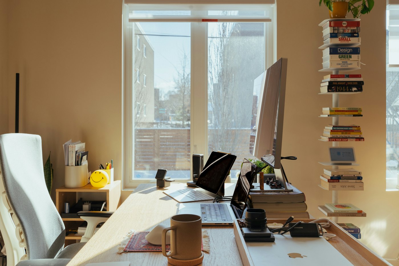 A sunlit desk with a computer, books and a plant