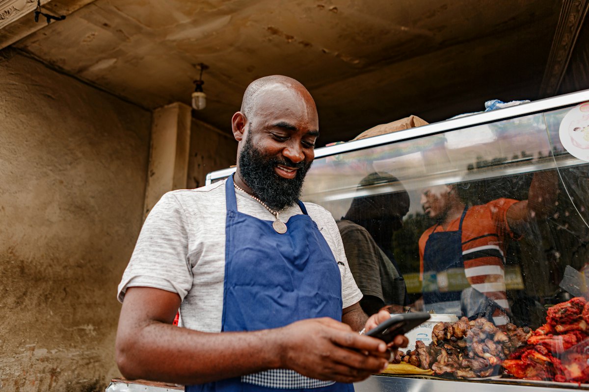 A food vendor in an apron checking his phone at his stall