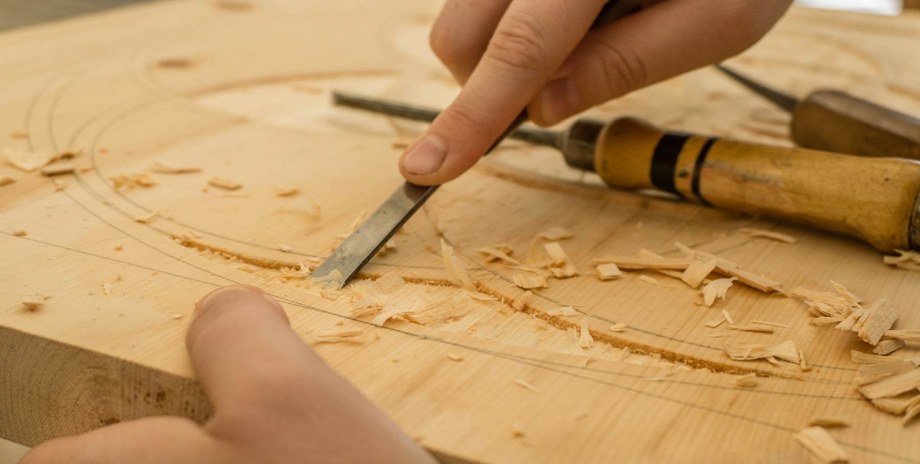 Hands guiding a chisel through a block of pale timber