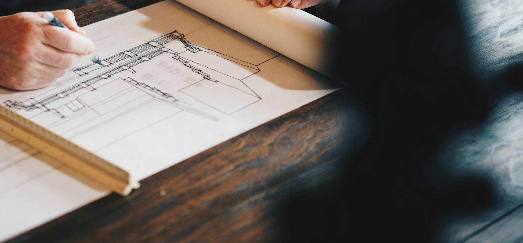 Hands sketching a house elevation with a scale ruler