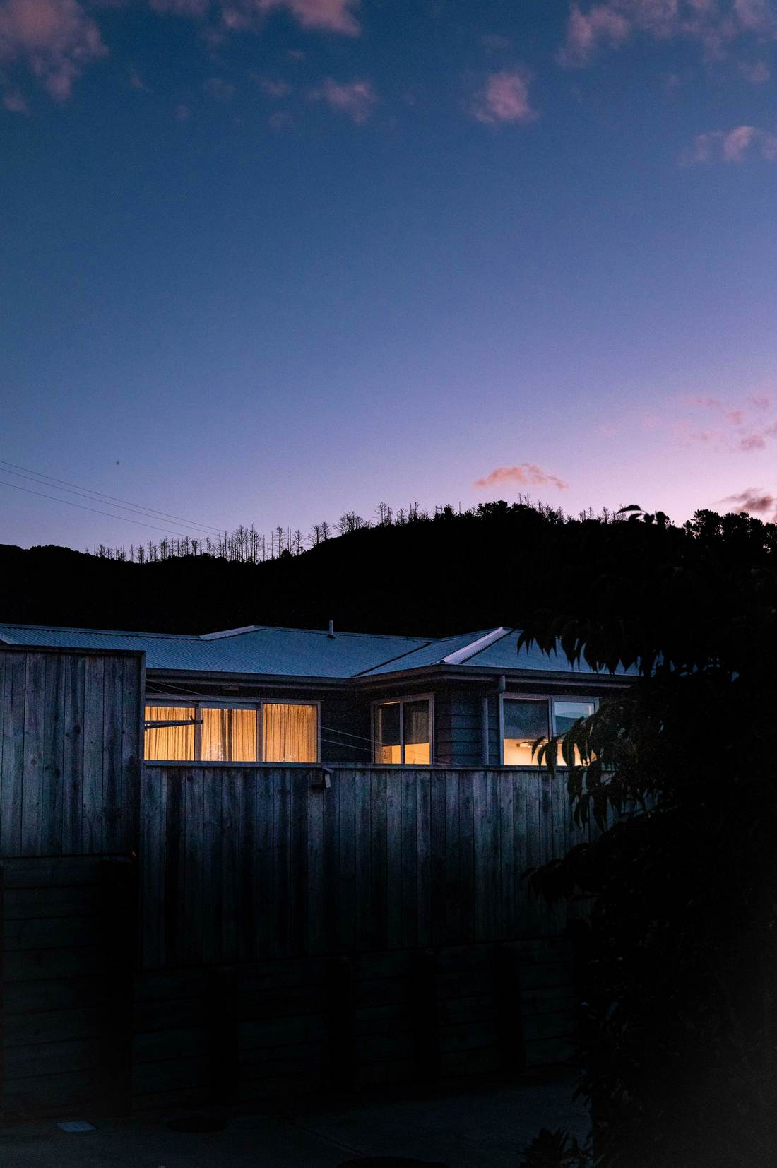Low timber house at dusk below a wooded hill