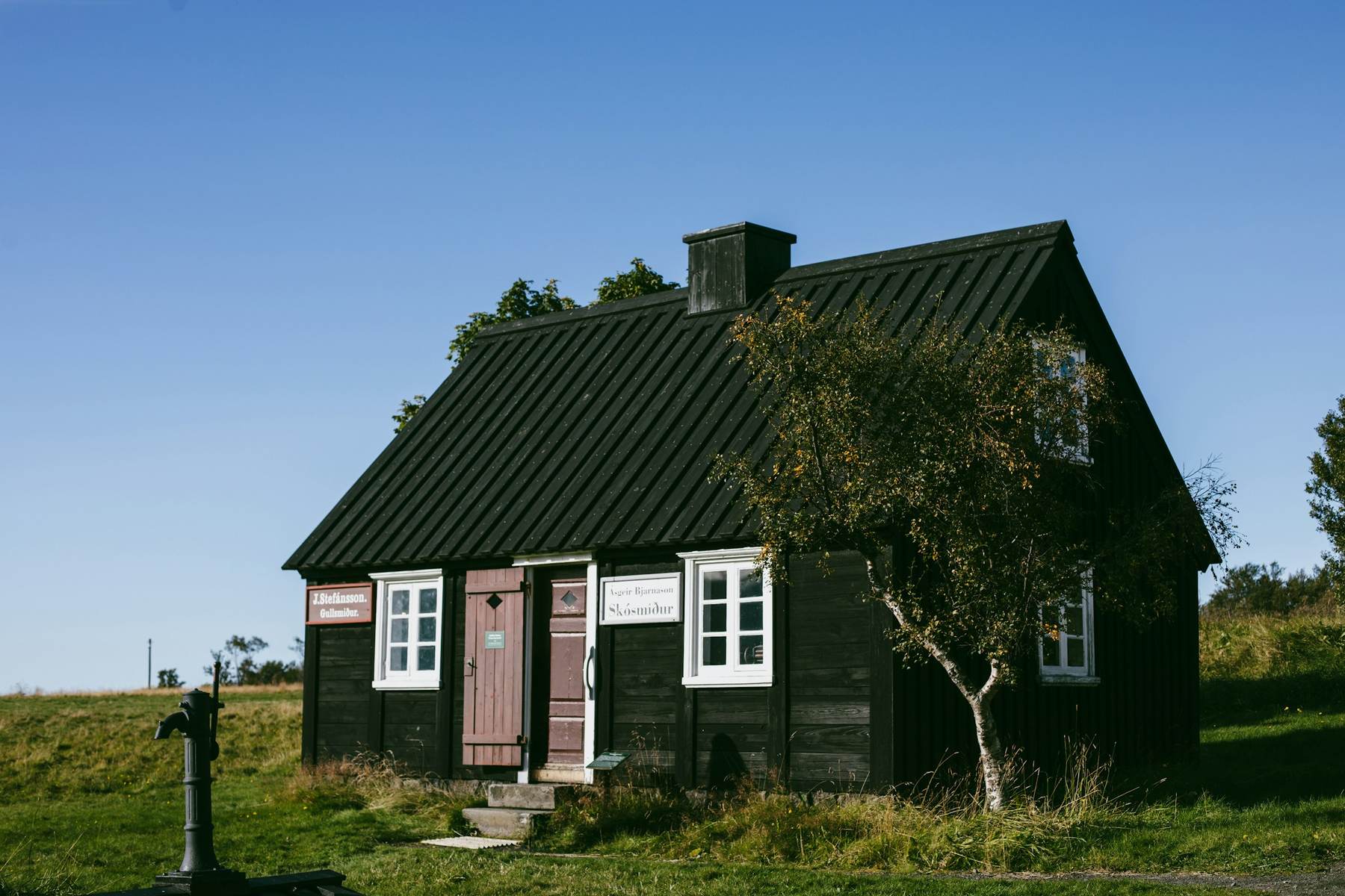 Dark timber cottage with a steep roof standing alone in a green field