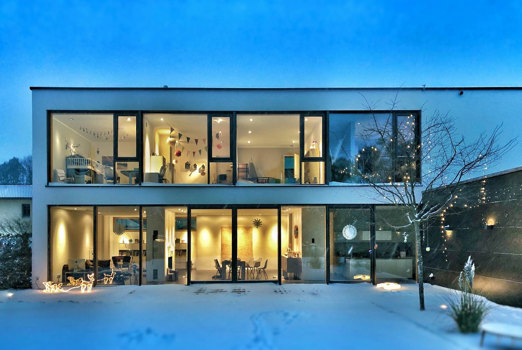 Glass walled modern home lit from inside on a snowy evening
