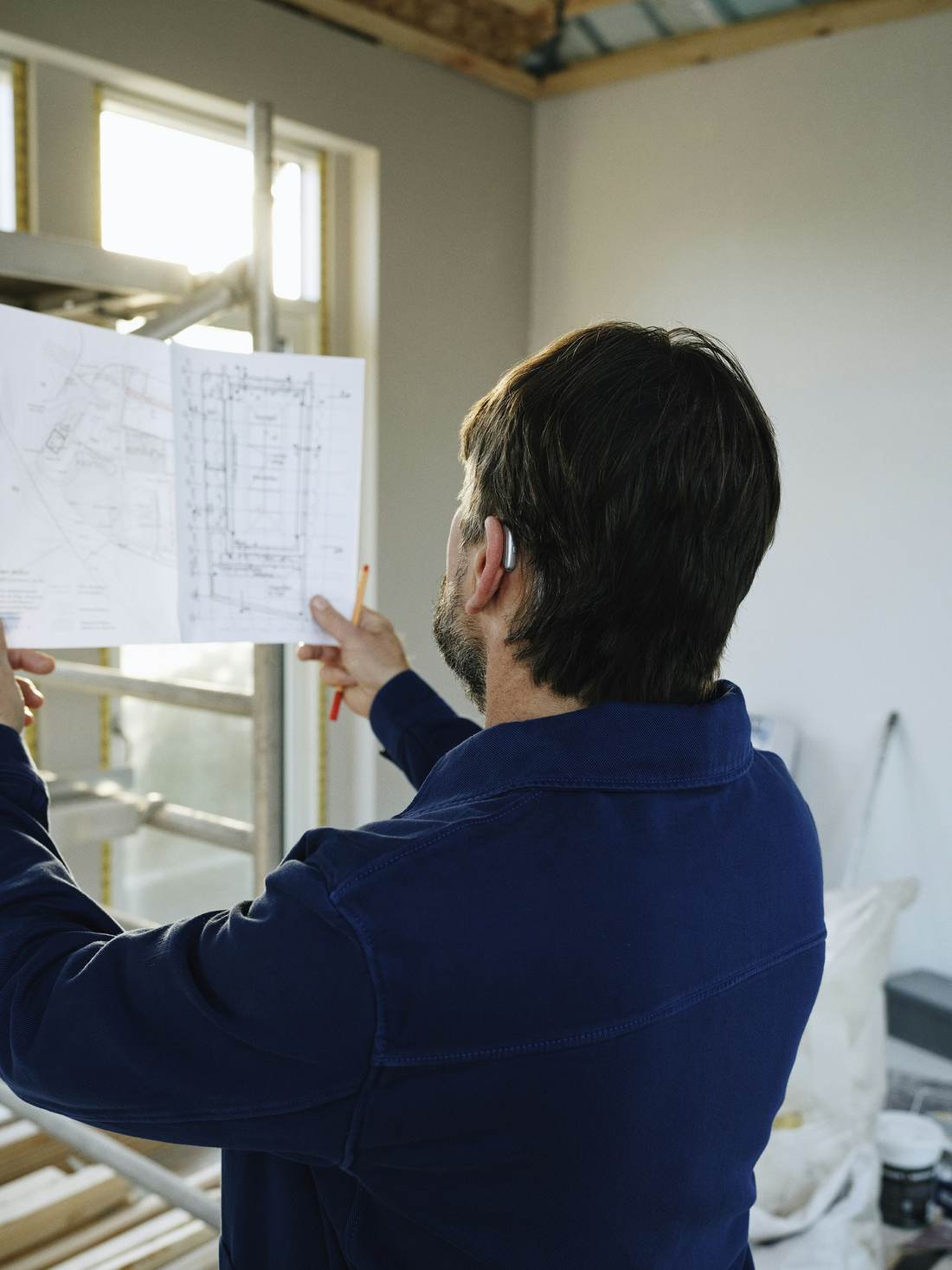 Builder holding up a drawing at a site window