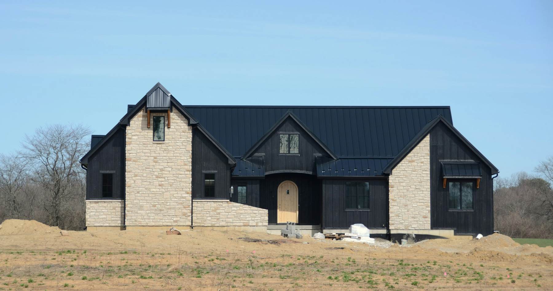 Black modern farmhouse with stone walls on an open lot