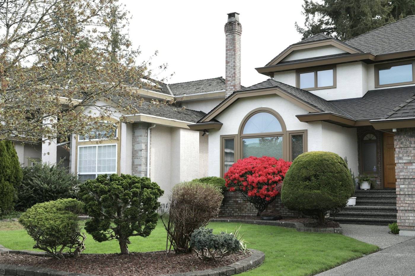 A front yard with clipped shrubs, red azaleas and a neat lawn leading to the front steps