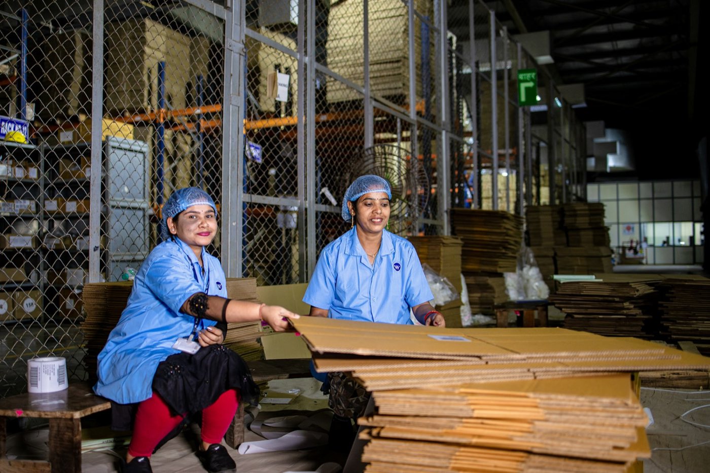 Two workers in hairnets and aprons at a workbench on a small factory floor