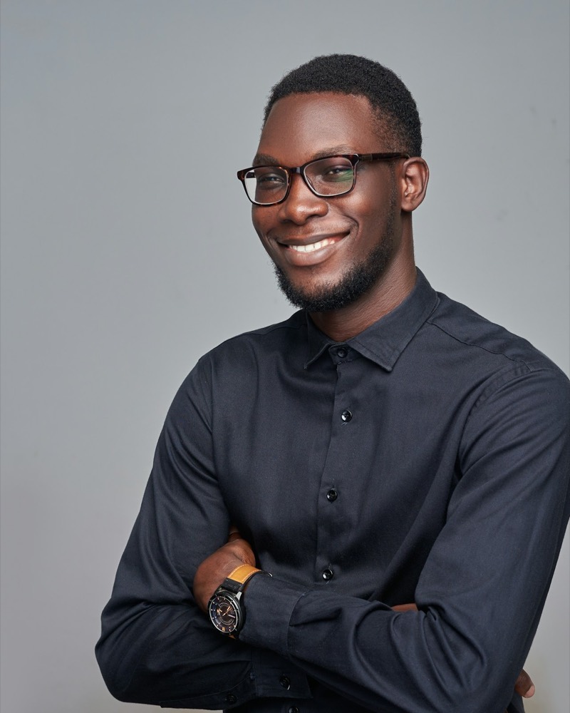 Portrait of Daniel Osei, smiling, arms crossed, in a dark shirt and glasses