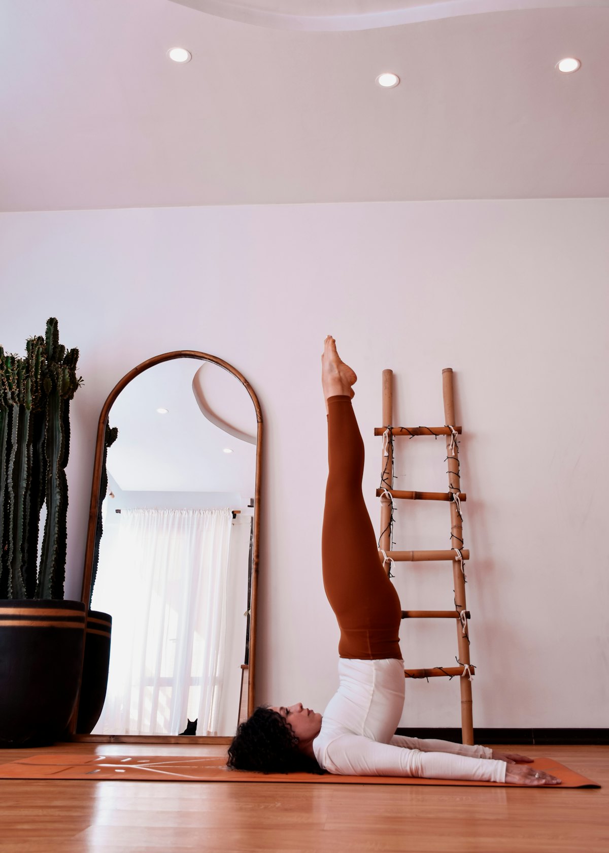 A woman in a shoulder stand on a mat in a soft, blush-toned room