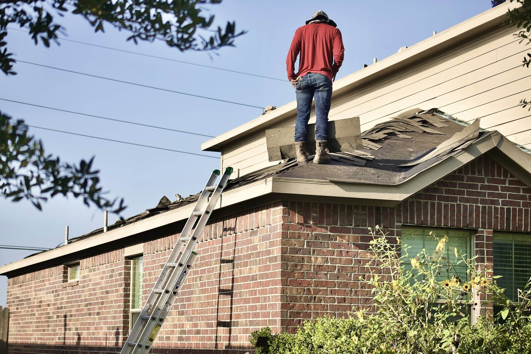 Roofer standing on a damaged roof above a brick wall