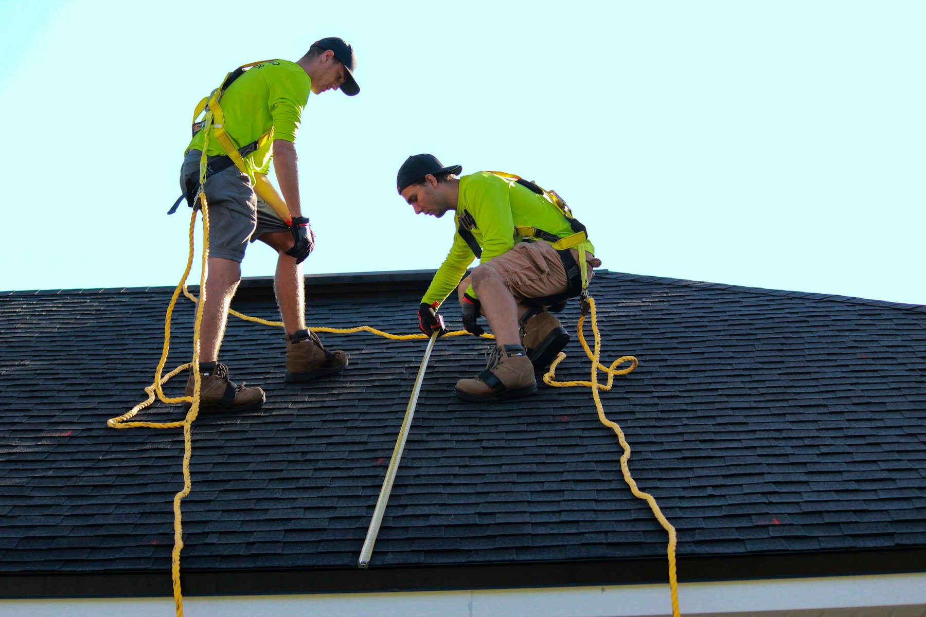Two roofers in hi-vis shirts and harnesses inspecting a roof