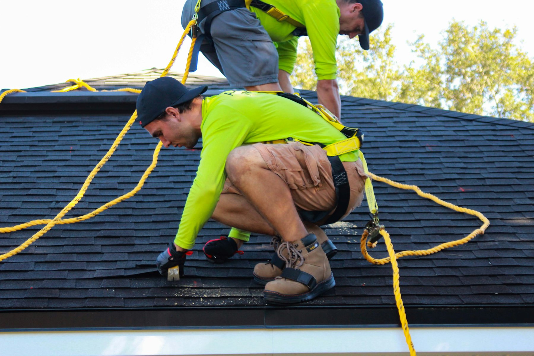Two roofers in hi-vis shirts and harnesses working on a shingle roof