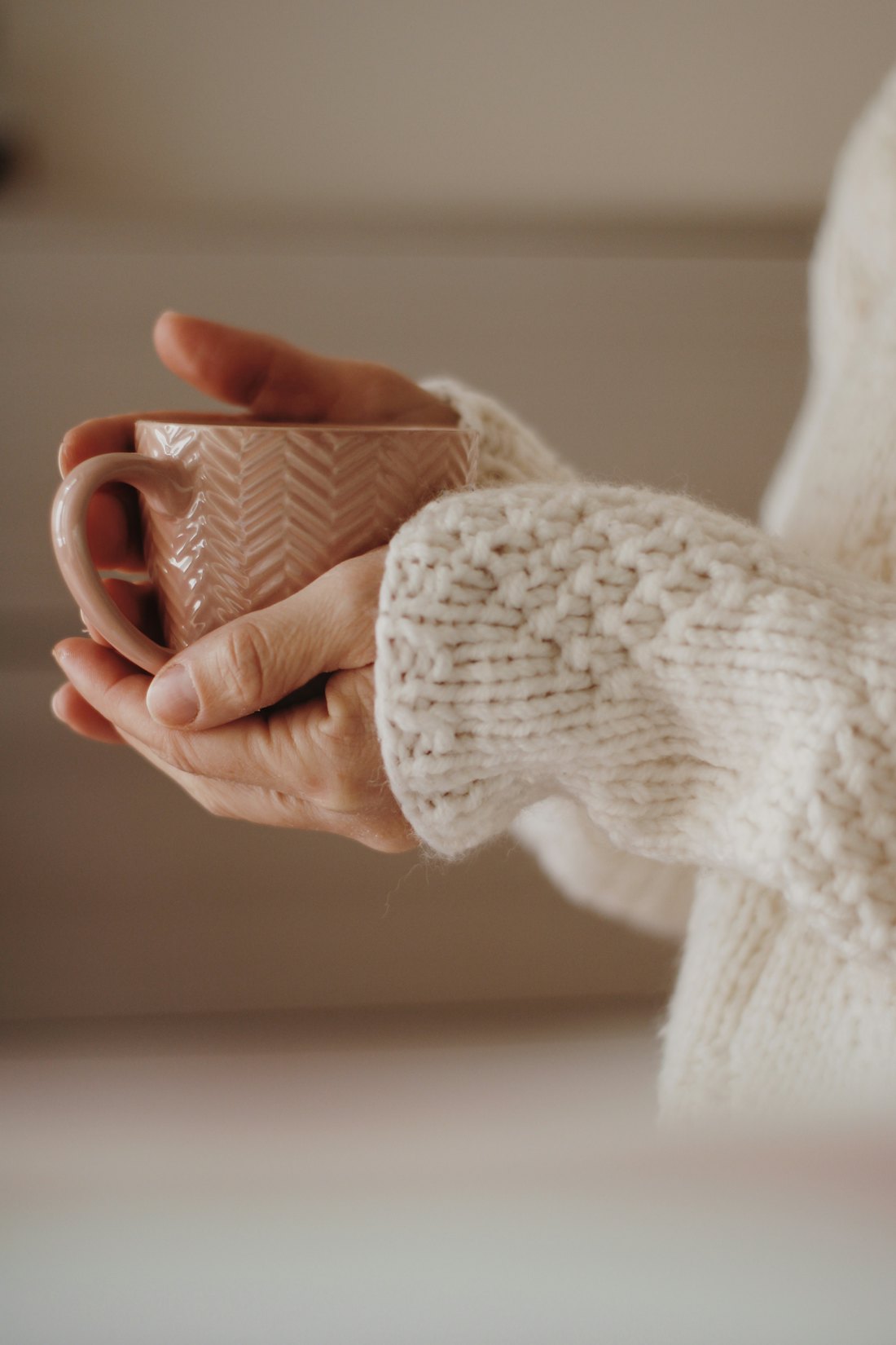 Hands in a cozy knit sweater wrapped around a warm mug