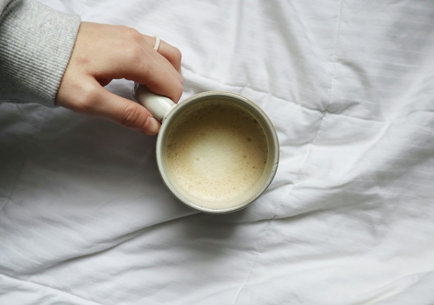 A hand holding a mug of tea on soft white bedding