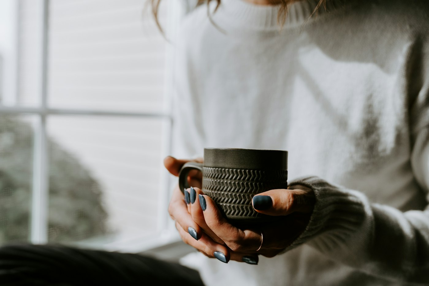 Hands in a soft sweater holding a warm cup of coffee