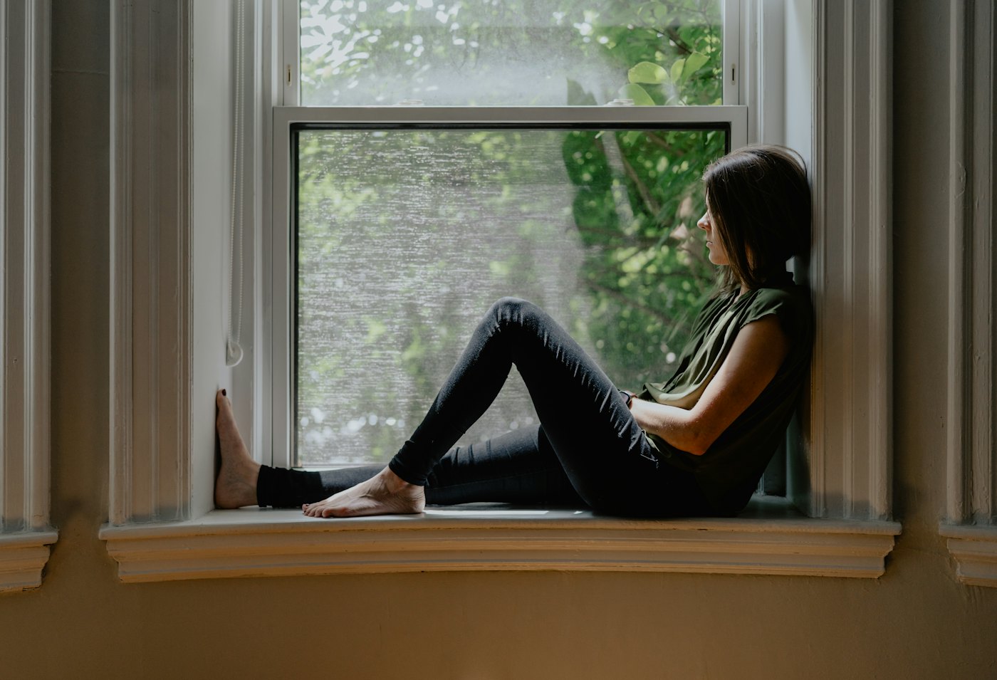 A woman sitting on a sunny window seat, looking outside