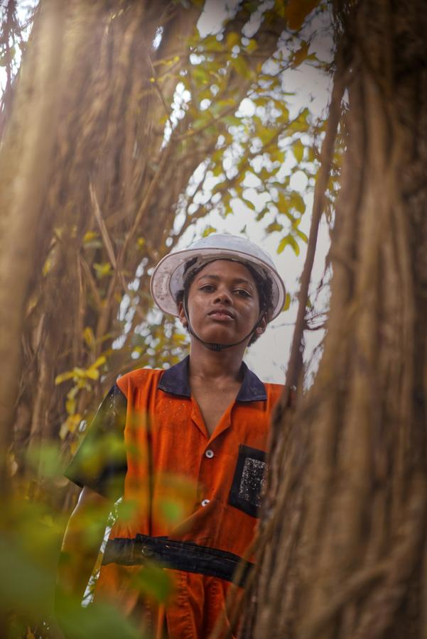 A crew member in a white helmet and orange vest beside a tree